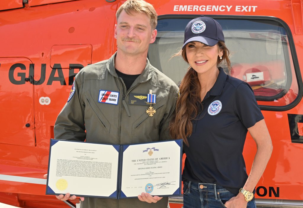 Department of Homeland Security Secretary Kristi Noem with Petty Officer 3rd Class Scott Ruskan, an aviation survival technician assigned to Air Station Corpus Chrisi, after Ruskan was awarded the Distinguished Flying Cross Medal in Kerrville, Texas, July 11, 2025. Secretary Noem presented the certificate to recognize Ruskan's “actions, skill and heroism” during aircrew 6553's support of numerous rescues in the wake of the devastating flash flooding near Kerrville. (U.S. Coast Guard photo illustration by Petty Officer 2nd Class Brandon Hillard)