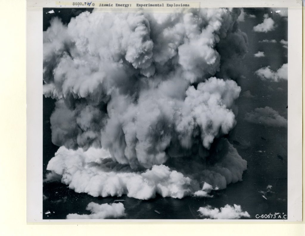 A massive explosion cloud spreads over the ocean with the taped on caption Atomic Energy Experimental Explosions