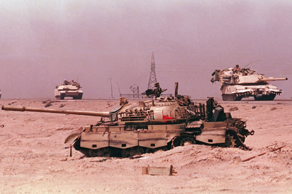 a wrecked Iraqi Type 69-II Main Battle Tank (MBT) abandoned beside a road as American M1A1 Abrams tanks drive past after the liberation of Kuwait during the Gulf War, Iraq, 1991. (Photo by Allan Tannenbaum/Getty Images)