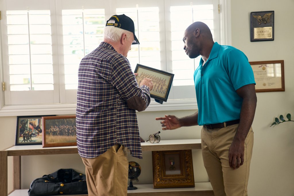 Veteran with African American caretaker friend with war memorabilia behind him