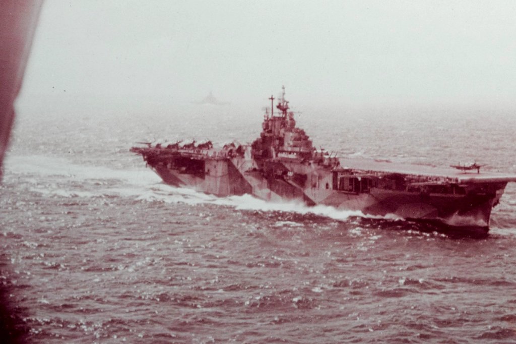 The U.S. Navy aircraft carrier USS Intrepid (CV-11) engaged in flight operations as viewed from the backseat of an Curtiss SB2C Helldiver during the Battle of Leyte Gulf. Another SB2C from Bombing Squadron 18 (VB-18) is launching from the carrier. Note the battleship in the distance.