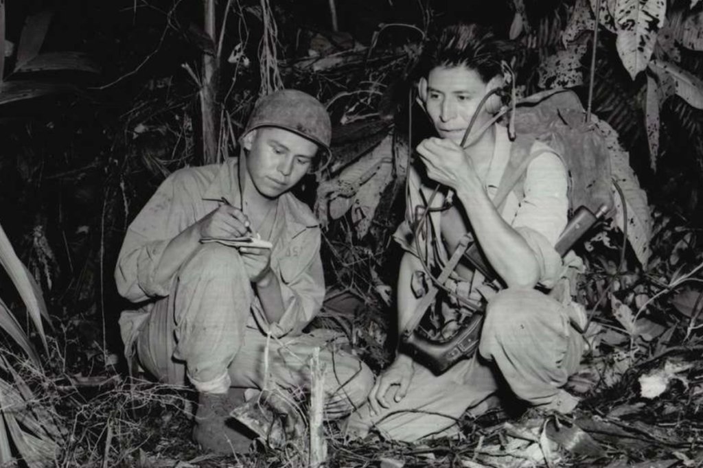 Cpl. Henry Bake, Jr., and Pfc. George H. Kirk, Navajos serving in December 1943 with a Marine Corps signal unit, operate a portable radio set in a clearing that they have hacked in the dense jungle close behind the front lines.
