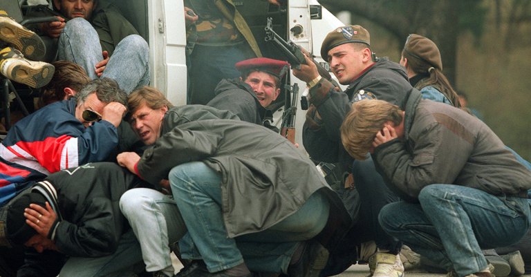 A Bosnian special forces soldier returns fire 06 April 1992 downtown Sarajevo as he and civilians come under fire from Serbian snipers. The Serb extremists were shooting from the roof of a hotel at a peace demonstration of some of 30,000 people as fighting between Bosnian and Serb fighters escalated in the capital of Bosnia-Hercegovina. (Photo credit should read MIKE PERSSON/AFP via Getty Images)