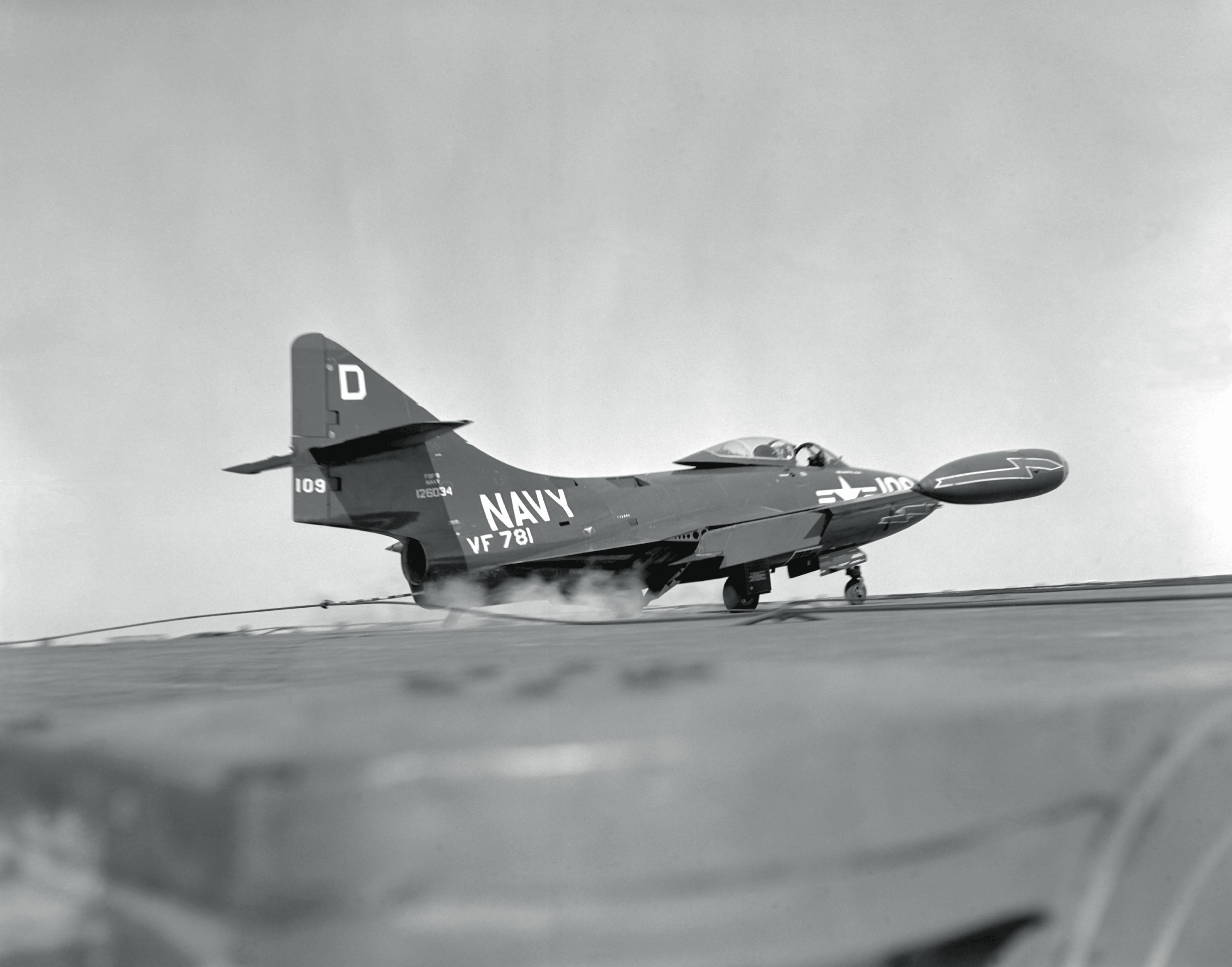 Lt. Joseph J. MacBrien, (RCN) Exchange pilot, serving with fighter sqdn. 781, USN, aboard USS ORISKANY (CVA-34) off coast of Korea. As he touches down, tail hook of F9F Panther jet engages an arresting wire and smoke comes from tires due to remendous friction. NARA FILE #: 80-G-448885