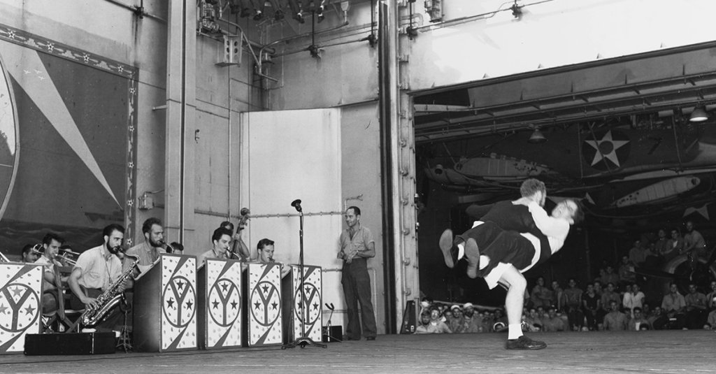 USS Yorktown (CV-5) with the “A Chart of the Cruises of USS Yorktown” mural behind the band during the Yorktown Jamboree on April 10, 1942, while the ship was in the Coral Sea. Image courtesy of Naval History and Heritage Command.
