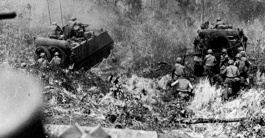 A combined arms operation in Vietnam. M113s clear the way through heavy bushes while infantry follows.