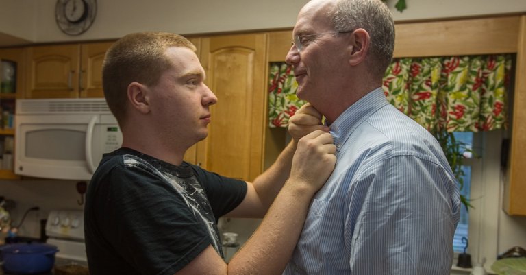 John Bucknam, 18, who has autism, draft buttons the top button of his dad Mark's shirt, July 25, 2014 in Rockville, MD. John like all shirt buttons to be closed. The Bucknam's have a series of locks on their doors to keep John from wandering off. (Photo by Evelyn Hockstein/For The Washington Post via Getty Images)