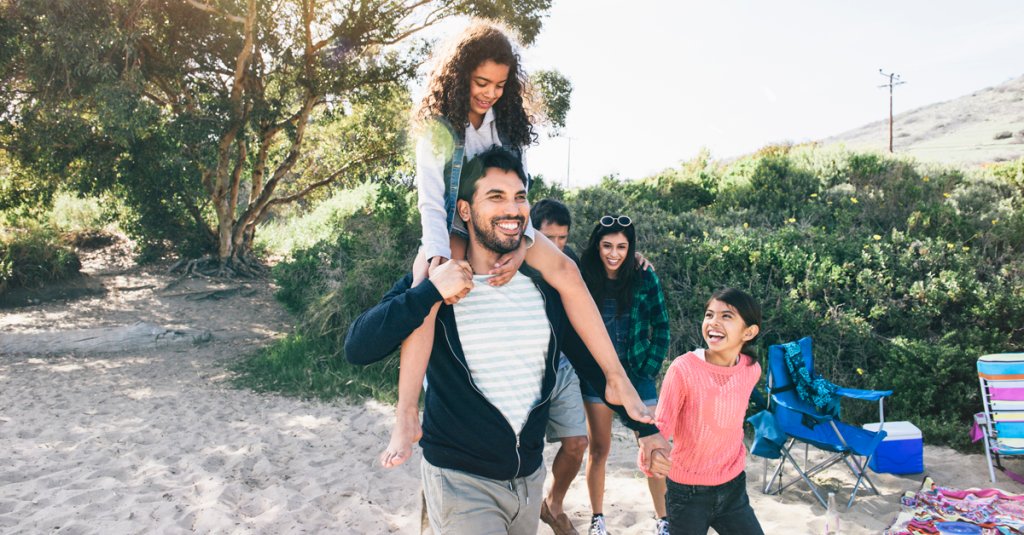 Smiling father carrying daughter on shoulders while walking at beach