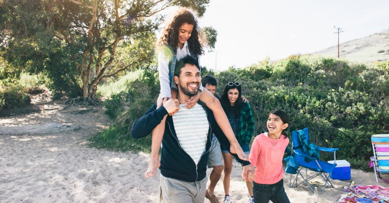 Smiling father carrying daughter on shoulders while walking at beach