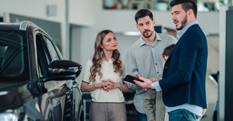 veterans buying a car: Car salesman explaining new vehicle features to a young family with a child at the dealership showroom