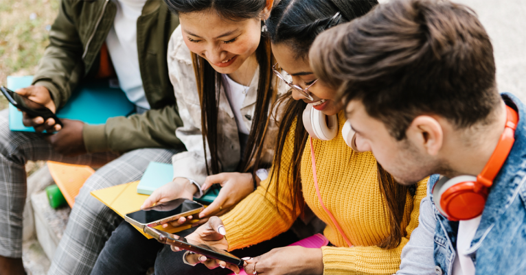 Diverse young teenage students having fun using mobile phone in college campus