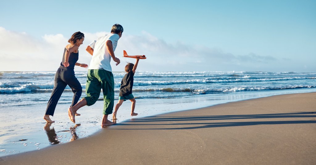 Parents running behind a boy running straight ahead with a model airplane held high in one hand.