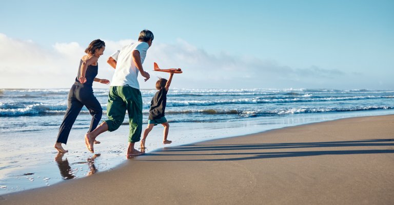 Parents running behind a boy running straight ahead with a model airplane held high in one hand.
